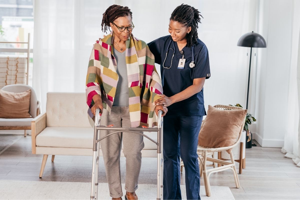 Nurse supporting an older woman using a walker during home rehab