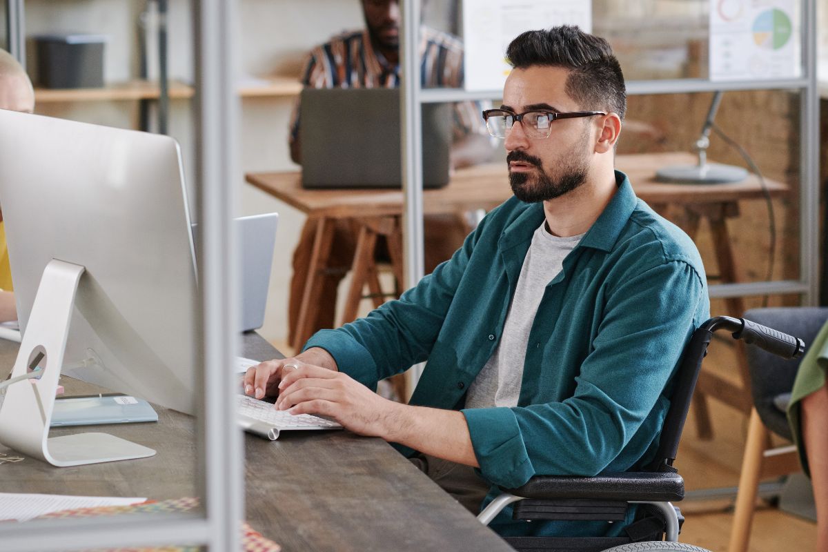Man using a wheelchair typing at a desktop computer in a modern office