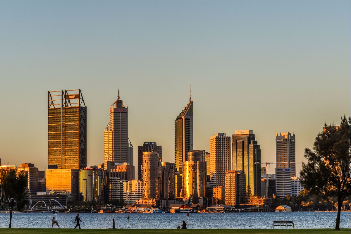 Perth skyline at golden hour across the Swan River, people walking along the foreshore