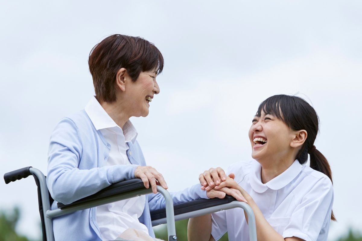 Carer laughing with an older woman who is using a walker outdoors