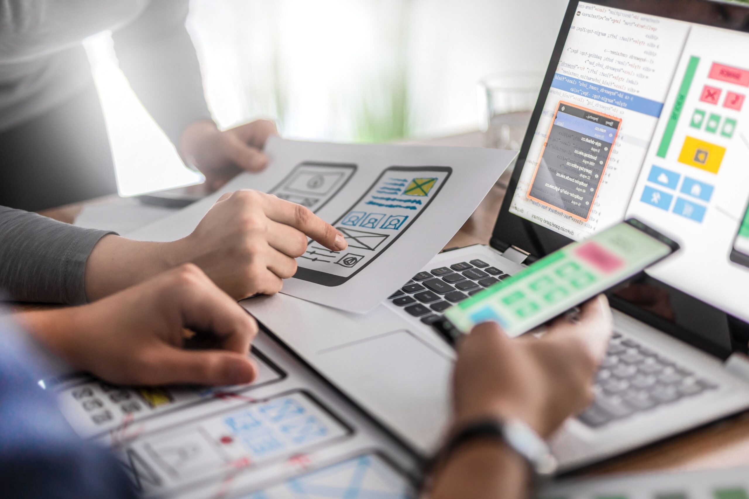 Designers reviewing mobile app wireframes with a laptop and smartphone on the desk