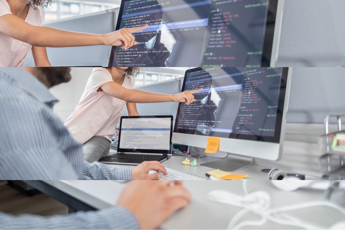 Developer typing while a colleague points to code on a large monitor beside a laptop