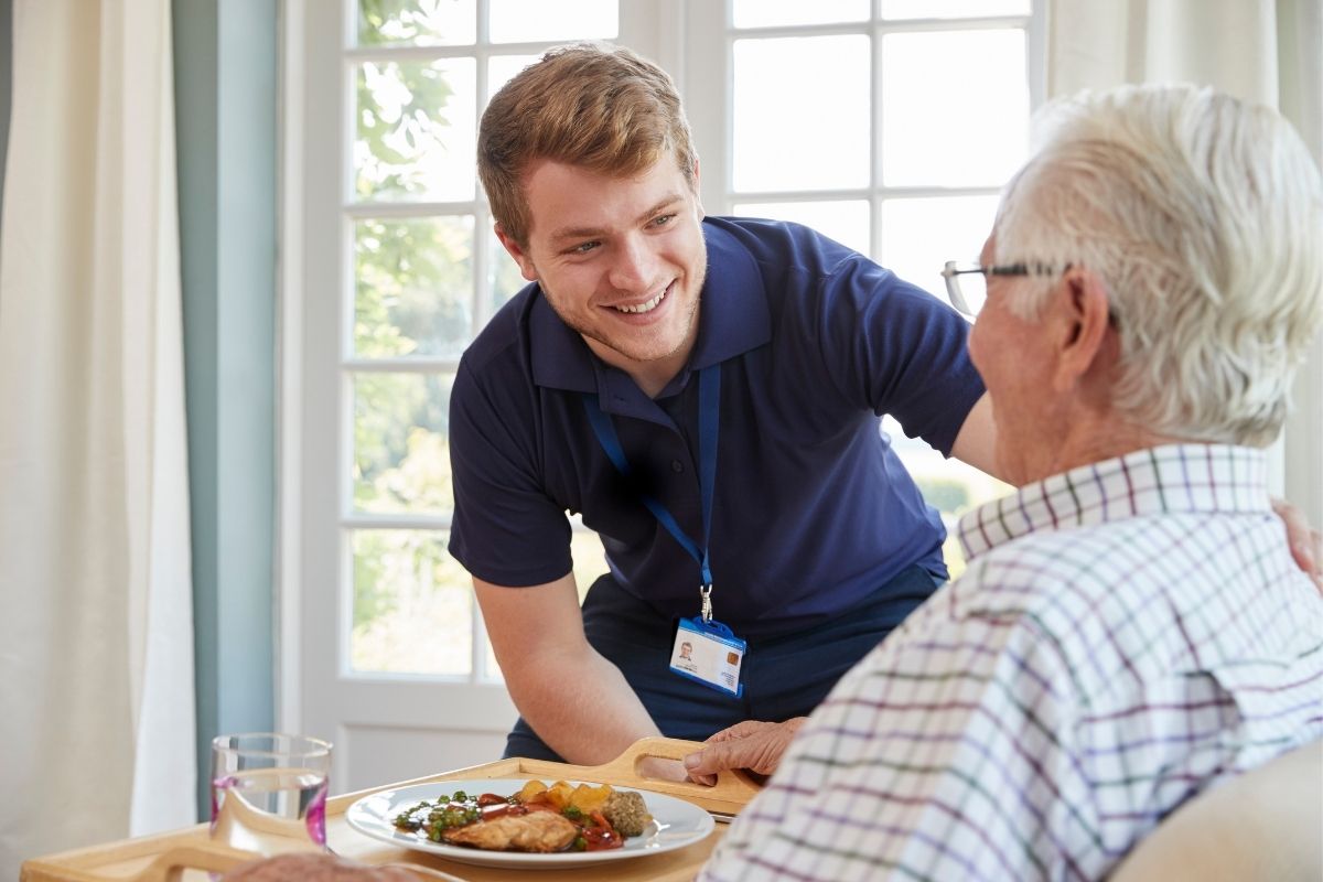 Support worker smiling while serving lunch to an older man at home