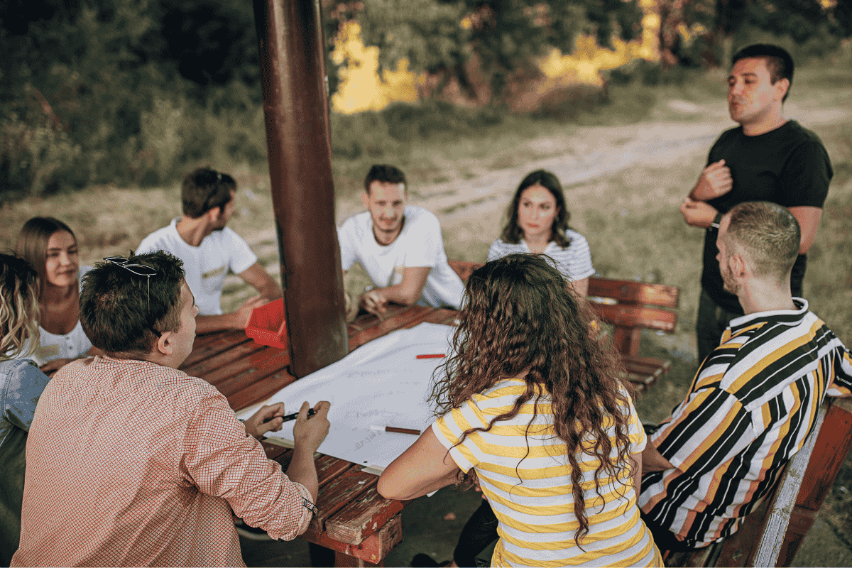 A group of people sitting outdoors around a table having a discussion.